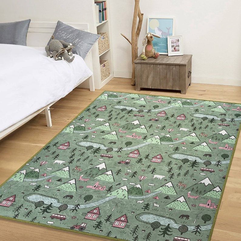 May include: A green and pink area rug with a whimsical design featuring mountains, trees, houses, and other woodland elements. The rug has a light green background with pink accents and a light green border.