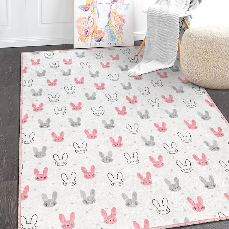 May include: A white and pink area rug with a repeating pattern of gray and pink bunny faces. The rug has a pink border.