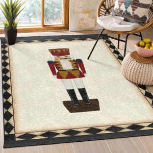 May include: A rectangular rug with a cream-coloured centre featuring a nutcracker design. The nutcracker is in red, gold, and black. The rug has a black border with a geometric pattern.