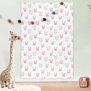 May include: A white background with a repeating pattern of pink and gray bunny faces. The bunnies have black eyes and whiskers. The background is dotted with small white dots.