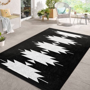 May include: Black and white geometric area rug with a fringe border. The rug has a modern design with white triangles on a black background.