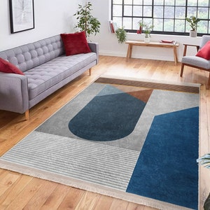 May include: Abstract geometric rug with a grey background, blue and brown shapes, and a white fringe border.