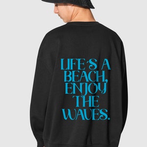 Puede incluir: Sudadera negra con un estampado gráfico azul que dice "Life's a beach, enjoy the waves."