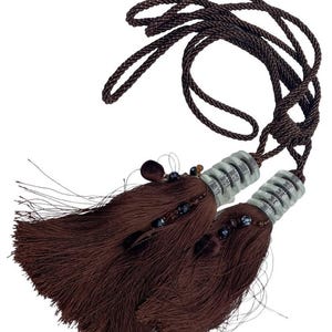 Può includere: Due fermatende a nappa marroni con dettagli argentati e un cordoncino intrecciato. Le nappe sono realizzate in un materiale morbido e sfilacciato e sono decorate con piccole perline. Questi fermatende sono progettati per tenere le tende.