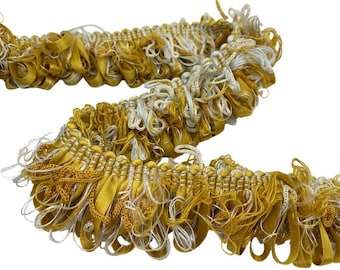 May include: Decorative trim in shades of gold and cream. The trim features a looped design with a fringe of loose threads. This textile trim is suitable for various craft and sewing projects, adding a touch of elegance.