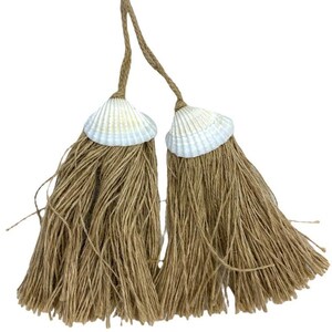 Può includere: Due nappe decorative a tema costiero. Ogni nappa presenta una conchiglia naturale attaccata a un fascio di spago marrone. Lo spago forma un fondo sfrangiato e le conchiglie sono bianche e color crema.