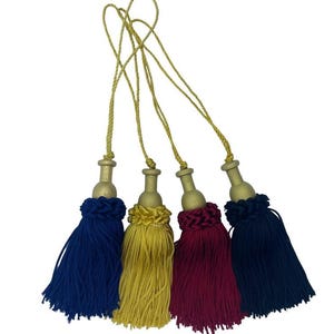 Peut inclure: Quatre glands décoratifs de couleur bleu marine, or, bordeaux et bleu marine foncé. Chaque gland a un dessus doré et un cordon torsadé doré pour l'accrochage. Les glands sont disposés sur un fond blanc.