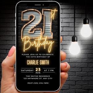 以下が含まれることがあります： 画面に21歳の誕生日パーティーの招待状が表示された黒いスマートフォン。招待状には、ネオンライトで照らされた木製の数字21、