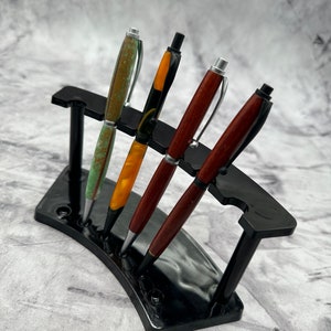 May include: Four wooden pens with different colored patterns are displayed in a black pen holder. The pens are arranged in a curved shape.