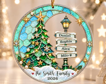 May include: A circular Christmas ornament featuring a stained-glass style design with a green pine tree, a street lamp with signs reading Daniel, Sophia, Alex, and Milo, and text at the bottom reading The Smith Family 2026 with two red hearts.