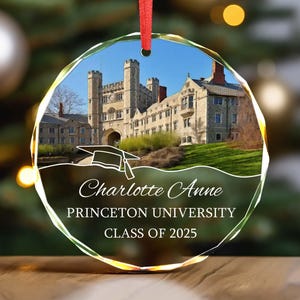 May include: A clear, faceted glass ornament with a red ribbon. The ornament features a photo of a university building and the text "Charlotte Anne, Princeton University, Class of 2025."