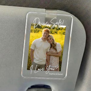 May include: Clear acrylic car visor accessory with a photo of a couple in a field. The text "Drive Safe!" and "I Love You" are written on the acrylic. The names "Sophia & Daniel" are also included.
