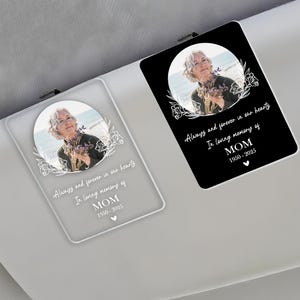 May include: A white car visor clip with a black background and a photo of a woman. The text reads "Always and forever in our hearts. In loving memory of MOM 1950-2025".