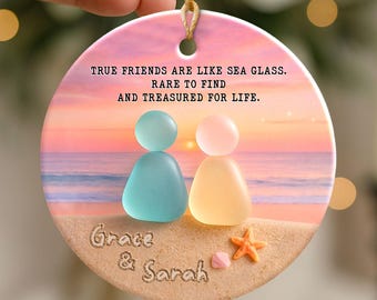 May include: A round ceramic ornament with a beach scene, featuring two figures made of sea glass. The ornament has the text "TRUE FRIENDS ARE LIKE SEA GLASS. RARE TO FIND AND TREASURED FOR LIFE." and the names "Grace & Sarah."
