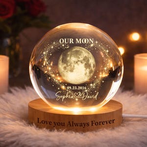 May include: A clear glass sphere lamp featuring a 3D laser-engraved moon, the text "OUR MOON", the date "09.23.2016", and the names "Sophia & David". The sphere rests on a round wooden base engraved with the text "Love you Always Forever".