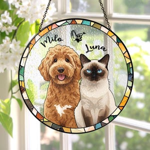 May include: Round stained glass window art featuring a brown dog and a Siamese cat with blue eyes. The names "Milo" and "Luna" are written above the pets. The window is framed with a colorful mosaic pattern and hangs from a chain.