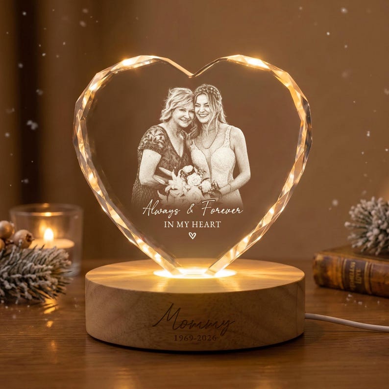 May include: A heart-shaped crystal plaque featuring a laser-etched photograph of two people, with the text "Always & Forever IN MY HEART" and a small heart icon. The crystal sits on a round wooden base engraved with "Mommy 1969-2026".