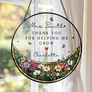 May include: Round stained glass window art with a black metal frame, hanging by a chain. The text reads "Mrs. Smith, Thank You For Helping Me Grow, Charlotte." Features a floral border with butterflies and a red heart.