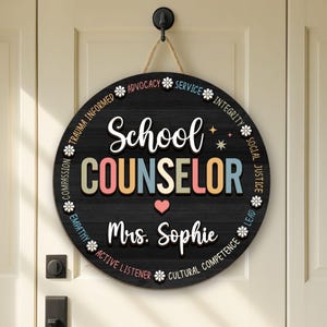 May include: Round black wooden sign for a school counselor. The sign reads "School Counselor" in colorful letters, with "Mrs. Sophie" below a heart. The sign includes words like "Advocacy" and "Empathy".