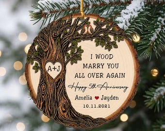Może przedstawiać: Okrągła drewniana ozdoba z ilustracją drzewa i wyciętym sercem z literami A+J. Tekst głosi: I WOOD MARRY YOU ALL OVER AGAIN, Happy 5th Anniversary, Amelia, Jayden oraz 10.11.2021. Na gałęzi siedzą dwa małe ptaszki.