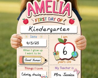 May include: A wooden sign for a child's first day of kindergarten, held by a person. The sign reads "AMELIA" in pink letters, "FIRST DAY OF Kindergarten", and includes sections for date, age, and teacher's name. The child is 6 years old.