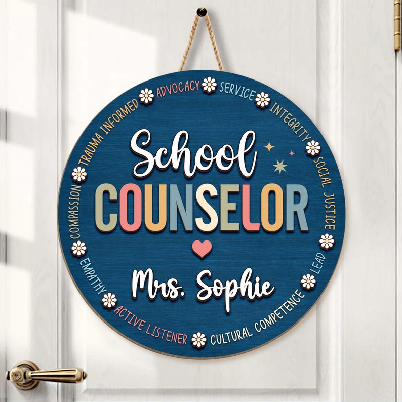 May include: A round, navy blue wooden sign with the words "School COUNSELOR" in colorful letters. The sign includes the name "Mrs. Sophie" and is decorated with floral accents and phrases like "Advocacy" and "Empathy". A jute rope is attached for hanging.