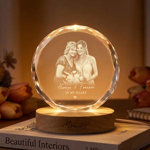 May include: A circular crystal plaque with faceted edges, laser-engraved with a portrait of two people and the text Always & Forever IN MY HEART. The crystal sits on a round wooden base engraved with the word Mommy and the years 1969-2026.
