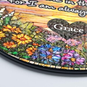 May include: A circular plaque featuring a stained-glass style floral design with yellow, orange, blue, and purple flowers. A dark heart-shaped overlay displays the word Grace. The background includes a sunset sky and text that reads for I am always.