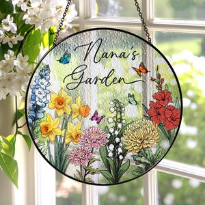May include: A round stained glass window hanging with a black metal frame. The glass features a colorful floral design with butterflies and the text "Nana's Garden".