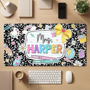 May include: A rectangular desk mat featuring a black and white composition notebook pattern background. The center displays a lined paper graphic with the text Mrs. HARPER, surrounded by colorful illustrations of a bow, globe, and school supplies.