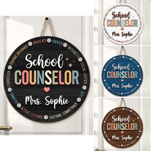 May include: A round wooden sign for a school counselor, featuring the words "School Counselor" in colorful letters. The sign includes the name "Mrs. Sophie" and decorative elements like hearts and stars. It hangs by a natural rope.