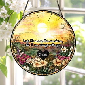 May include: A circular stained glass suncatcher featuring a yellow sunlit landscape with a field of colorful flowers. The text reads, "Look for me in the sunshine, for I am always with you," above a black heart shape containing the name "Grace."