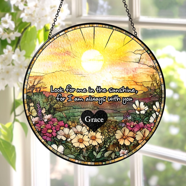 May include: A circular stained glass suncatcher featuring a yellow sunlit landscape with a field of colorful flowers. The text reads, "Look for me in the sunshine, for I am always with you," above a black heart shape containing the name "Grace."