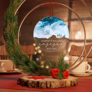 May include: A clear round ornament with a photo of ocean waves. The ornament has the text "HARPER & WILLIAM engaged 30.05.2023" printed on it.