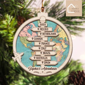 May include: A circular wooden ornament featuring a world map background and a central signpost with directional arrows labeled Mexico, Netherlands, Canada, France, Italy, Brazil, Australia, and Spain. It includes the text 2025 and Sophia's Adventures.