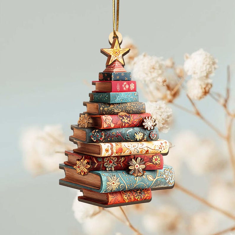 K&ouml;nnte beinhalten: Ein Weihnachtsbaumschmuck aus Holz in Form eines B&uuml;cherstapels. Die B&uuml;cher sind in verschiedenen Farben gehalten, darunter Rot, Blau und Braun, mit Blumen- und Sternmustern. Ein Holzstern sitzt oben, mit einem goldenen Faden zum Aufh&auml;ngen.