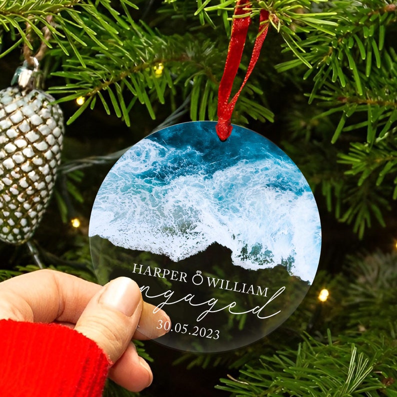 May include: Round clear glass ornament with a photo of ocean waves and the text "HARPER & WILLIAM engaged 30.05.2023" printed on it.