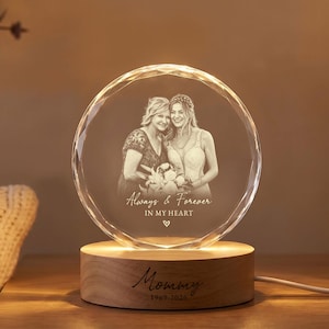 May include: A circular glass plaque with a faceted edge, laser-engraved with a portrait of two people and the text Always & Forever IN MY HEART. The plaque sits on a cylindrical wooden base engraved with the text Mommy 1969-2026.