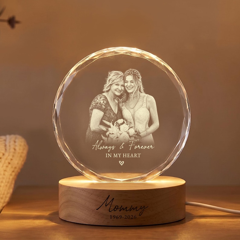 May include: A circular glass plaque with a faceted edge, laser-engraved with a portrait of two people and the text Always & Forever IN MY HEART. The plaque sits on a cylindrical wooden base engraved with the text Mommy 1969-2026.
