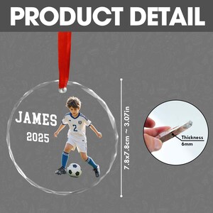 May include: A clear, round ornament with a photo of a young soccer player in a white and blue uniform, with the name "JAMES" and the year "2025". The ornament is 7.8x7.8cm (~3.07in) and 6mm thick, with a red ribbon for hanging.