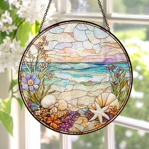 May include: Round stained glass window art depicting a beach scene with a blue ocean, sandy shore, and colorful flowers. The artwork includes seashells, a starfish, and a variety of floral elements. The window is suspended by a black chain.