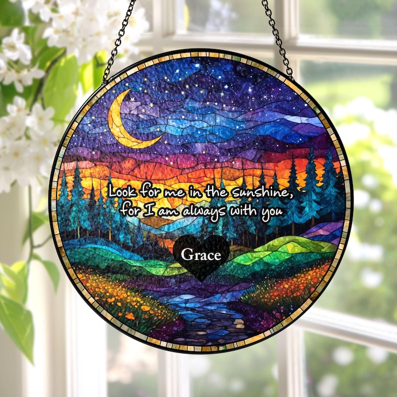 May include: A circular stained glass suncatcher featuring a landscape with a crescent moon, starry night sky, pine trees, and a stream. The text reads, "Look for me in the sunshine, for I am always with you" above a black heart labeled "Grace."