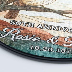 May include: A round decorative plaque with a black border. The plaque features the text "50TH ANNIVERSARY" and the names "Rosie & Gary" along with the date "10.20.1973". The background has a stained glass effect with brown, green, and white colors.
