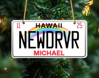 May include: A white license plate ornament with the text "HAWAII" above a rainbow graphic. The plate reads "NEWDRVR" in large black letters and "MICHAEL" in red. Numbers "11" and "25" are in the corners.