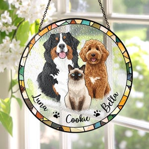 May include: A round, stained-glass window hanging featuring three pets: a Bernese Mountain Dog, a Goldendoodle, and a Siamese cat. The pets' names, Luna, Bella, and Cookie, are written on the glass. The window has a colorful mosaic border.