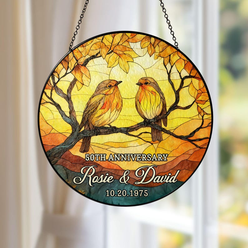 May include: Round stained glass window art featuring two birds perched on a branch, set against a warm, autumnal background. The design includes the text "50th Anniversary" and the names "Rosie & David" with the date 10.20.1975.