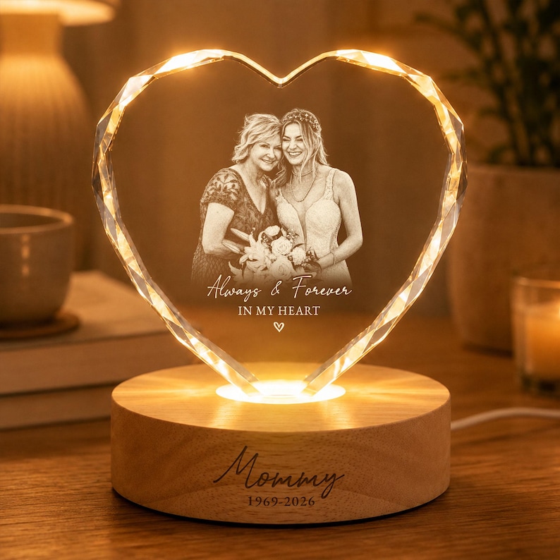 May include: A heart-shaped glass plaque with a laser-etched photograph of two people, featuring the text "Always & Forever IN MY HEART" and a small heart icon. The plaque sits on a round wooden base engraved with "Mommy 1969-2026" and glows.