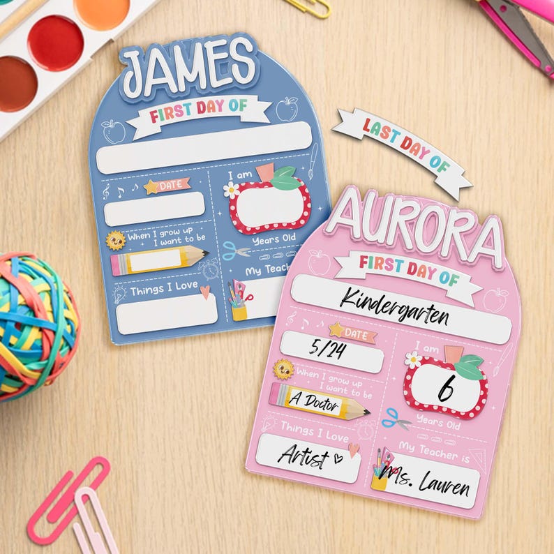 May include: Two colorful first day of school signs. One is blue with the name "JAMES" and the other is pink with the name "AURORA". Both signs have spaces for the date, age, and things they love.