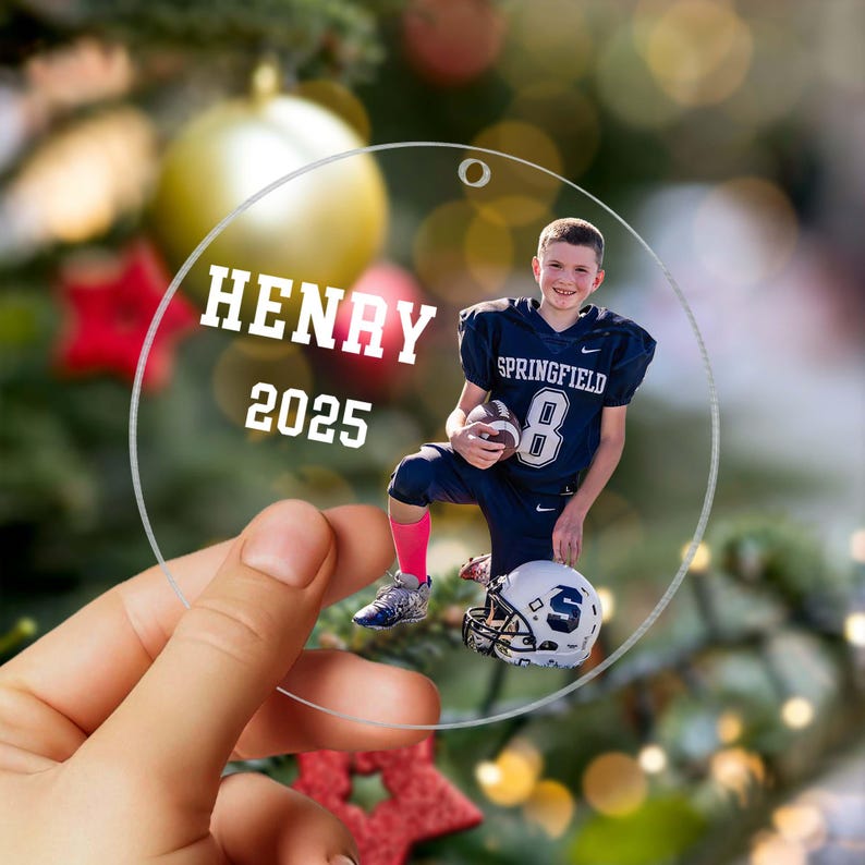 May include: Clear, round Christmas ornament with a photo of a young football player. The ornament has the name "HENRY" and the year "2025" printed in white. The player is wearing a navy blue uniform with the number "8".