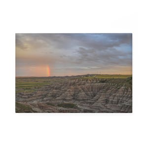 Puede incluir: Un arcoíris aparece sobre un paisaje de formaciones rocosas en capas, con un cielo nublado arriba.
